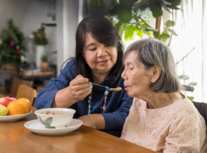 Daughter feeding elderly mother with soup at home.